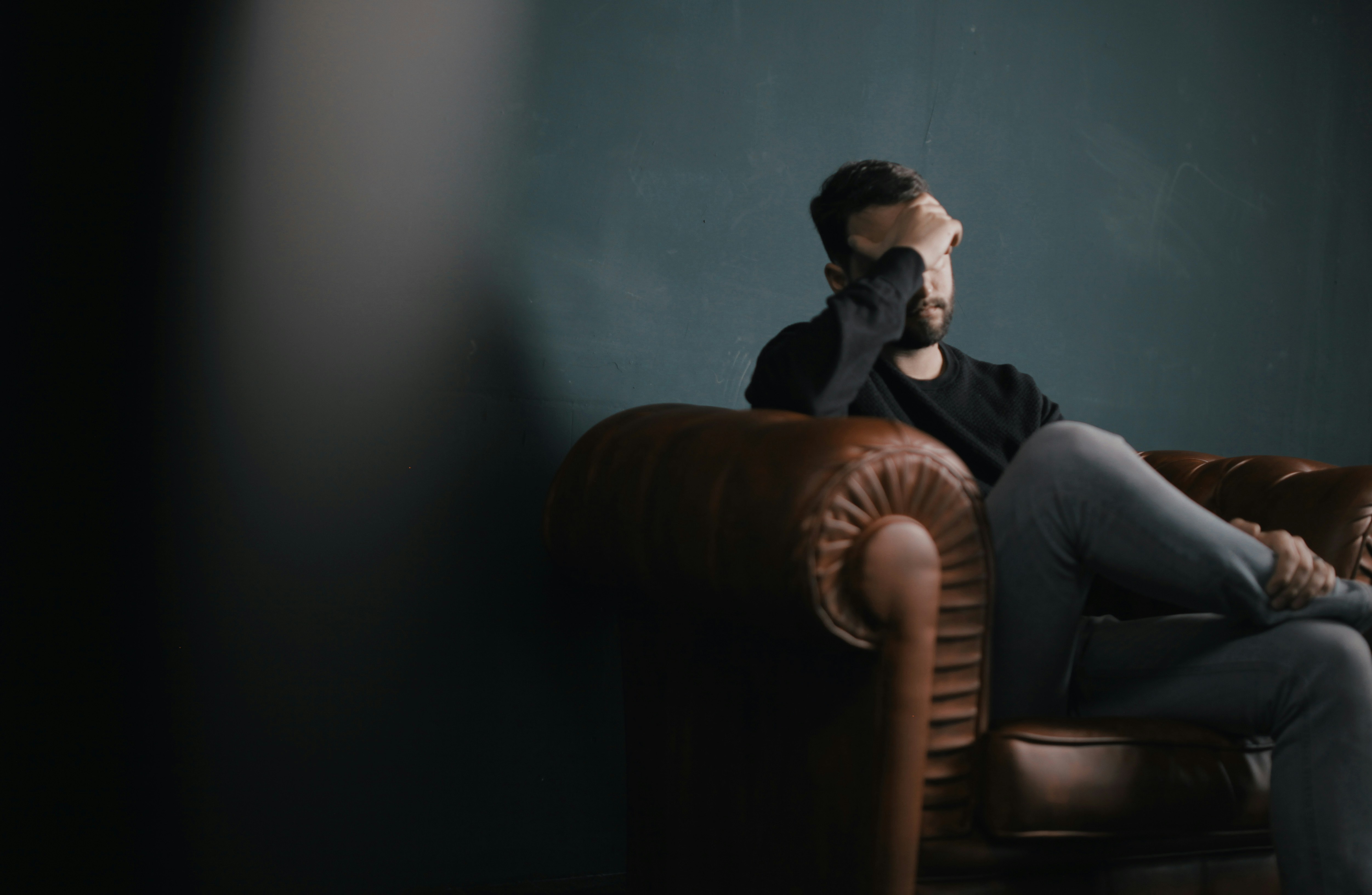 man sat in brown leather chair sad and in thought